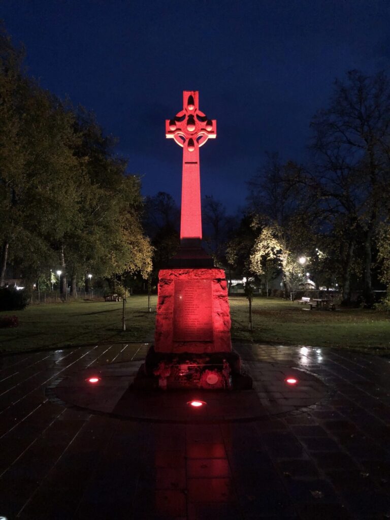 Night image of Kingussie War Memorial illuminated in red.